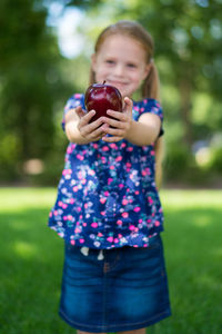 Smiling girl holding apple on field