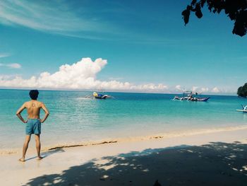 Rear view of man standing at beach against blue sky