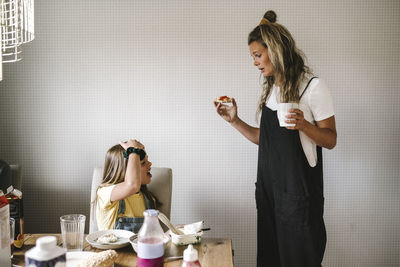 Daughter refusing to eat breakfast while mother standing by with coffee cup at home