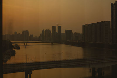 Bridge over river by buildings in city against sky