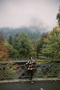Young woman standing on railing against trees