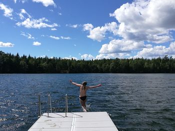 Shirtless girl diving into lake against blue sky