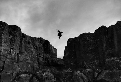 Low angle view of silhouette man jumping over rocks