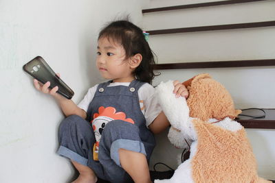 Cute baby girl playing phone cover while sitting on steps at home