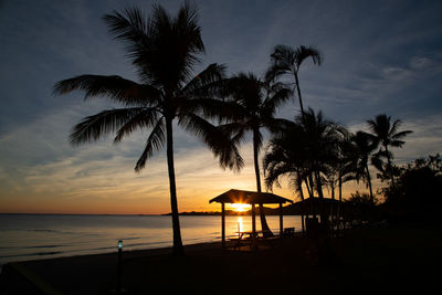 Silhouette palm trees by swimming pool against sky during sunset