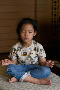 Full length of cute girl meditating while sitting at home