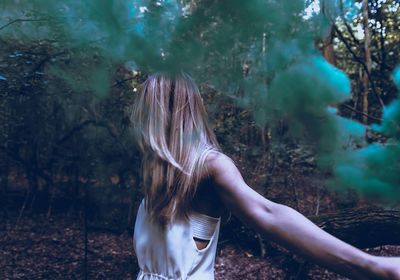 Young woman standing by green smoke in forest
