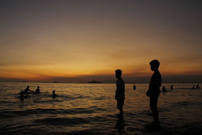 Silhouette people on beach against sky during sunset