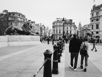 Rear view of people walking by lion statue at trafalgar square against sky