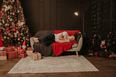 Young man fell asleep on couch near christmas tree. decorated house for new year. christmas morning. 