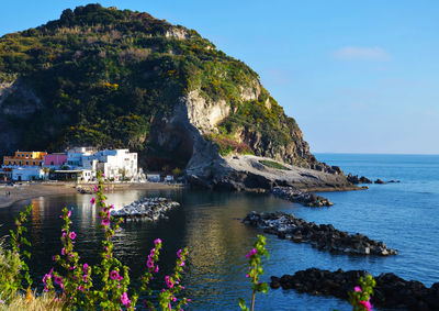 Scenic view of sea by mountain against sky