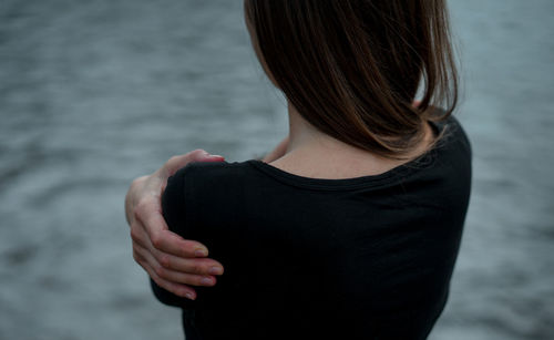 Rear view of woman touching her shoulder outdoors