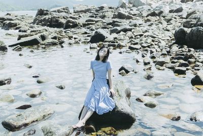 High angle view of beautiful woman blowing bubble gum while sitting on rock at beach