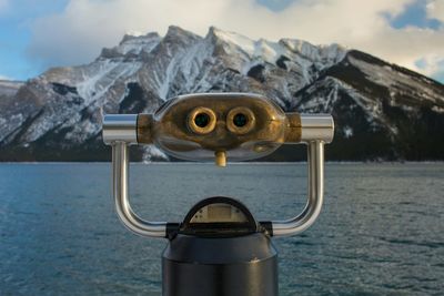 Close-up of coin-operated binoculars by sea against sky