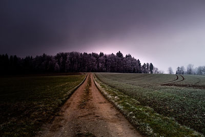 Dirt road amidst field against sky