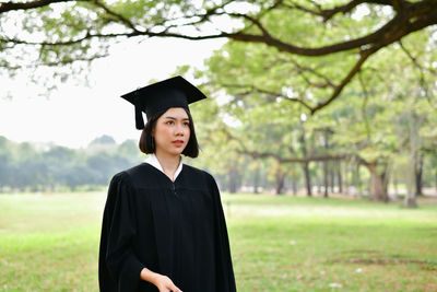 Student wearing graduation gown while standing on field at park