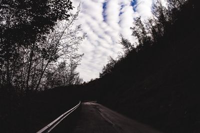 Empty road amidst silhouette trees against sky