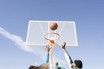 Male and female friends playing basketball on sunny day