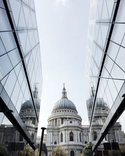 Low angle view of st paul cathedral amidst buildings with reflection against sky