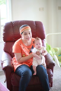 Portrait of smiling mature woman with son sitting on armchair