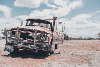 Abandoned car on field against sky