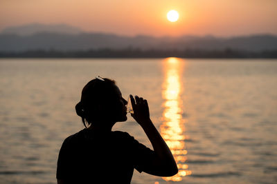 Silhouette man standing by sea against sky during sunset