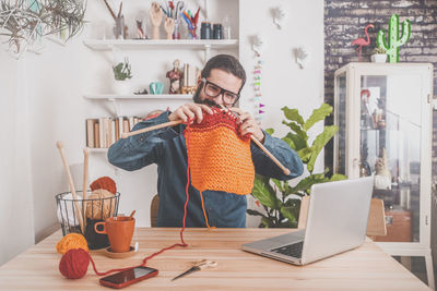 Bearded man knitting at home using laptop for watching online tutorial