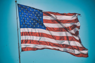 Low angle view of american flag waving against blue sky