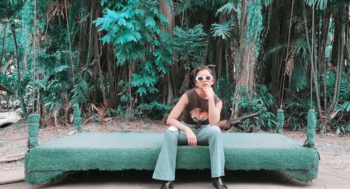 Portrait of woman wearing sunglasses sitting on seat against plants