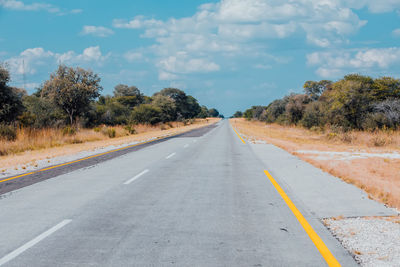 Empty road along trees and plants against sky