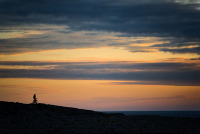 Silhouette person standing on rock against sky during sunset