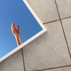 Reflection of hand and clear sky on mirror