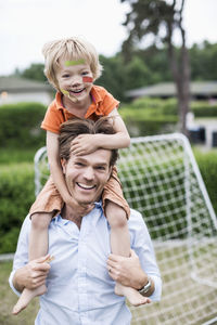 Portrait of happy father carrying injured boy on shoulders