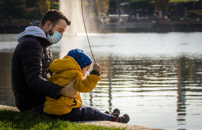 Father and son wearing masks sitting by lake