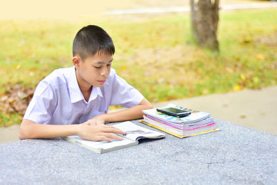 Boy reading book while sitting at park