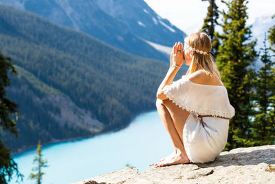 Side view of woman holding pine cone while standing against mountain