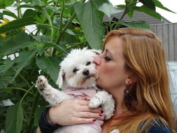 Young woman with long hair kissing dog by leaves