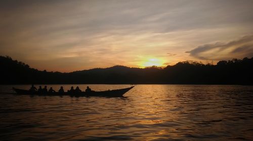 Silhouette people on boat in sea against sky during sunset