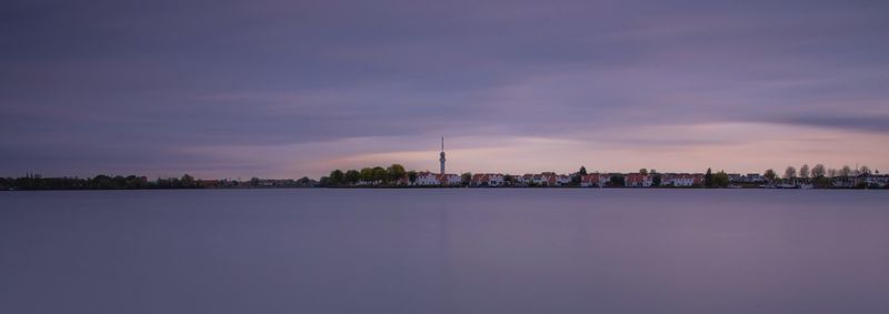 Scenic view of lake by buildings against sky during sunset