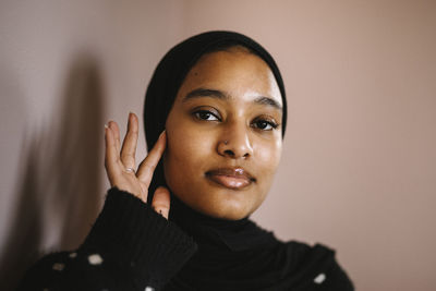 Young woman touching face against peach background