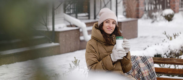 Cheerfully brunette woman drinking from flask outdoors in the city in winter. warming up, enjoying