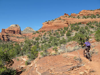 Rear view of woman riding bicycle on dirt road against clear sky