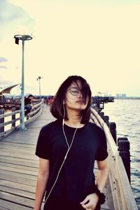 Young woman on pier by sea against sky