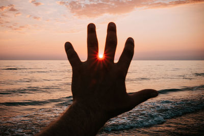 Human hand against sea during sunset
