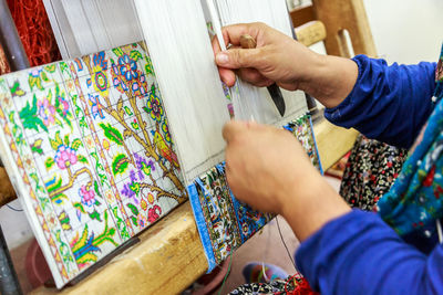 Midsection of woman weaving carpet in loom