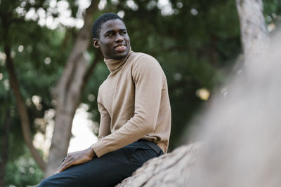 Portrait of young man looking away while sitting on tree