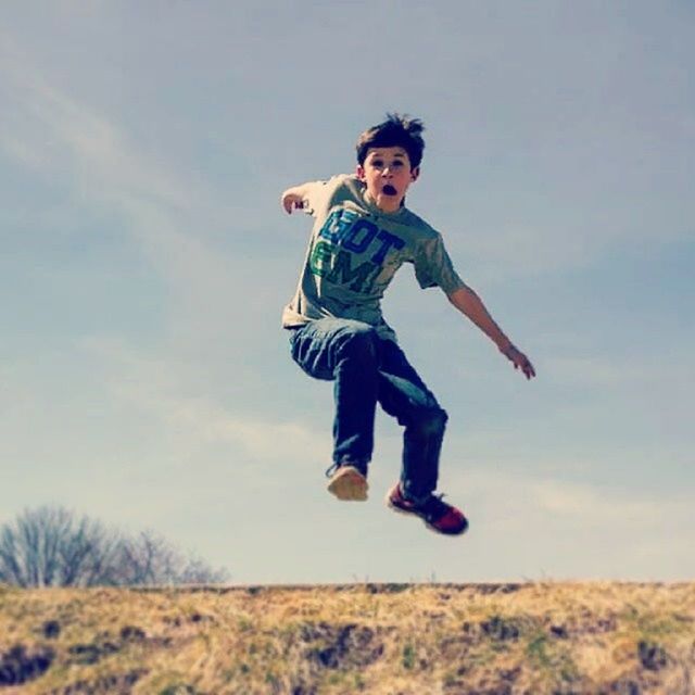 full length, leisure activity, lifestyles, casual clothing, person, sky, childhood, mid-air, looking at camera, portrait, fun, front view, happiness, smiling, elementary age, field, young adult, cloud - sky