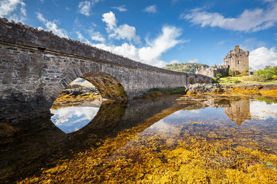 Arch bridge over river against cloudy sky