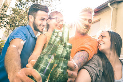 Low angle view of happy friends toasting drinks while standing against sky during sunny day