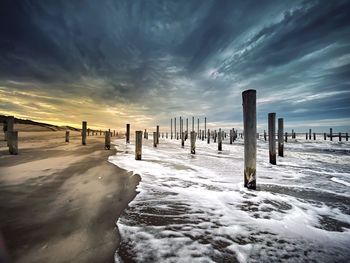 Wooden posts on a foam covered beach against sky during sunset